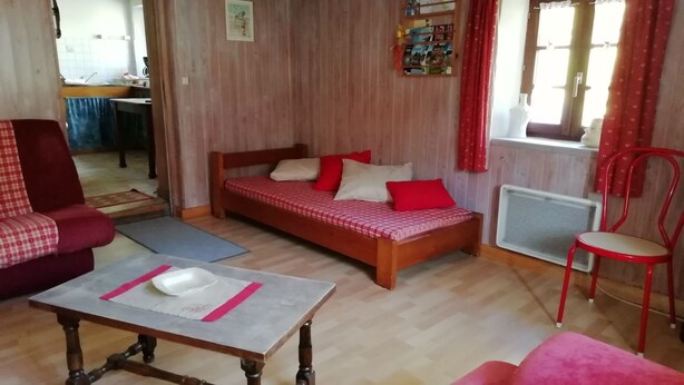 Una stanza con un letto di legno, una sedia rossa, un tavolo di legno e un divano rosso.
