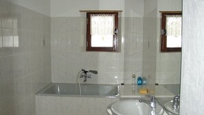 Un bagno con vasca, lavandino e finestra con tende di pizzo.