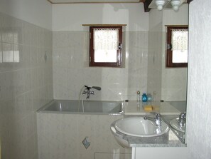 Ein Badezimmer mit einer Badewanne, einem Waschbecken und einem Fenster mit Spitzenvorhängen.