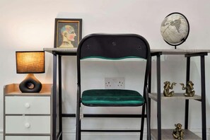 A chair with a green cushion, a desk with a globe and figurines, and a lamp on a bedside table. - Spacious 4-bedroom Apartment in Belvedere Sleeps 9 With Parking (Belvedere)