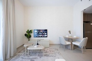 Ein modernes Hotelzimmer mit Flachbildfernseher, einem kleinen Esstisch, zwei Stühlen, einem weißen Sofa, einer Pflanze und einer Küchenzeile.