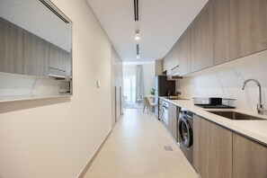 A modern kitchen with a washing machine, a sink, and a dining area in the background. - Bloomfields Studio in Fairways 3-YGC (Abu Dhabi)