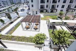 A rooftop patio area with tables and chairs, surrounded by greenery and a solar panel. - Bloomfields Studio in Fairways 3-YGC (Abu Dhabi)