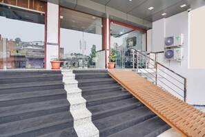 A modern building entrance with a staircase leading to a second floor, glass doors, and outdoor potted plants. - Hotel O Ajmer Central Grand Suman (Ajmer)
