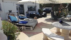 Un patio al aire libre con cama, sillas de descanso, una mesa y plantas en macetas.