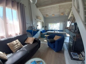 A living room with a black leather sofa, a blue armchair, and a dining area with a table and chairs. - Waterfront fisherman's cottage in a nature reserve; pets welcome (Sigean)