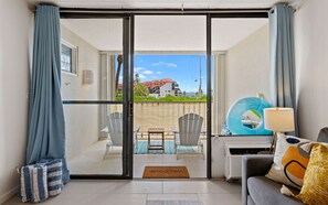 Une pièce dotée d’une porte-fenêtre coulissante donnant sur un balcon, ainsi que d’un canapé, d’une table et d’une chaise.