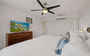 Ein Schlafzimmer mit einem Bett, einem Deckenventilator, einem Fernseher auf einer Kommode und einem Schrank mit Klappläden.
