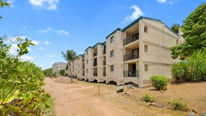 Um edifício residencial com várias andares e varandas, rodeado por vegetação e um caminho de terra.