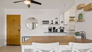 Uma cozinha moderna com armários brancos, uma mesa de jantar de madeira e um ventilador de teto.
