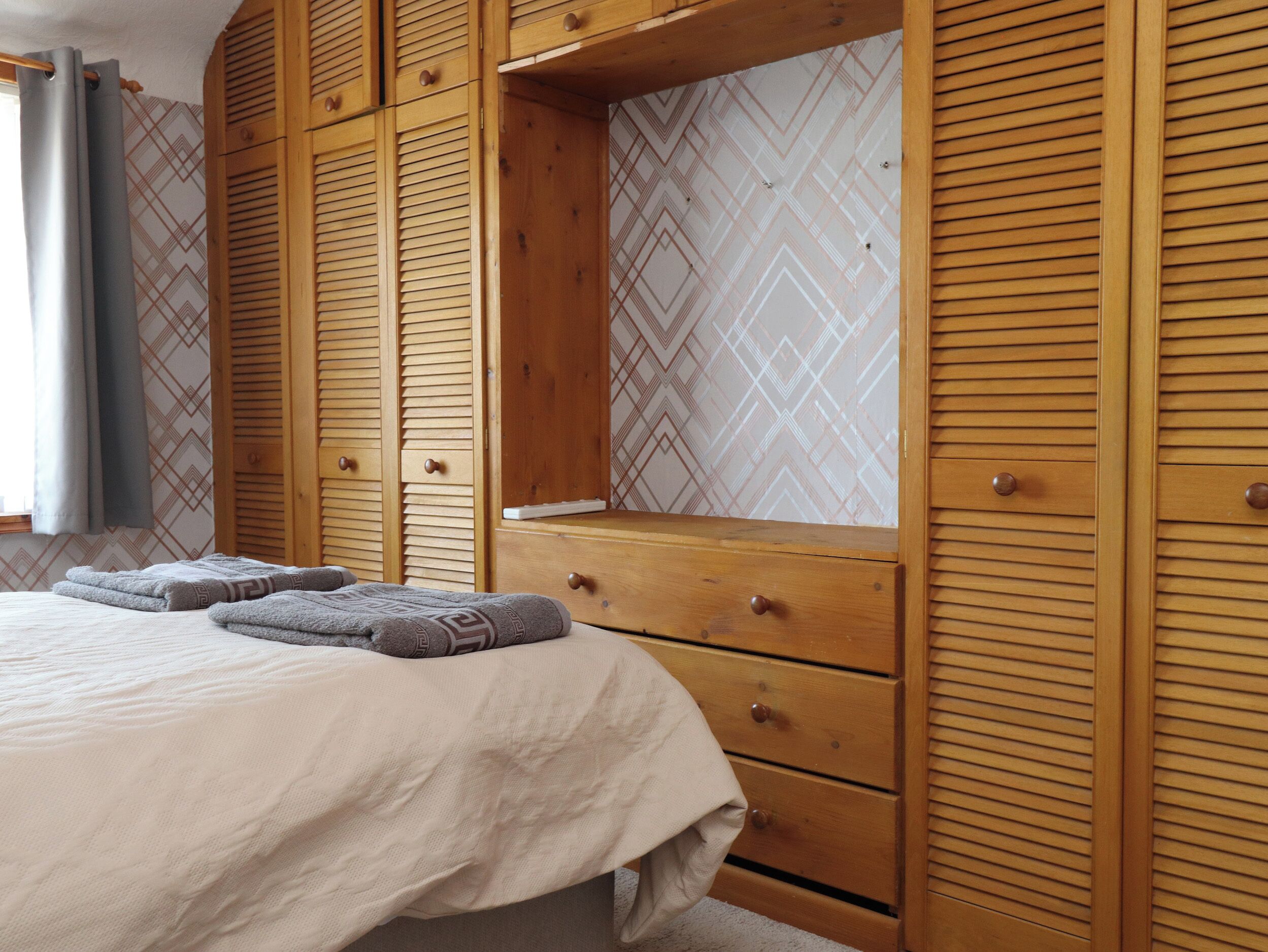 A bedroom with a bed, wooden wardrobe, and a window with curtains.