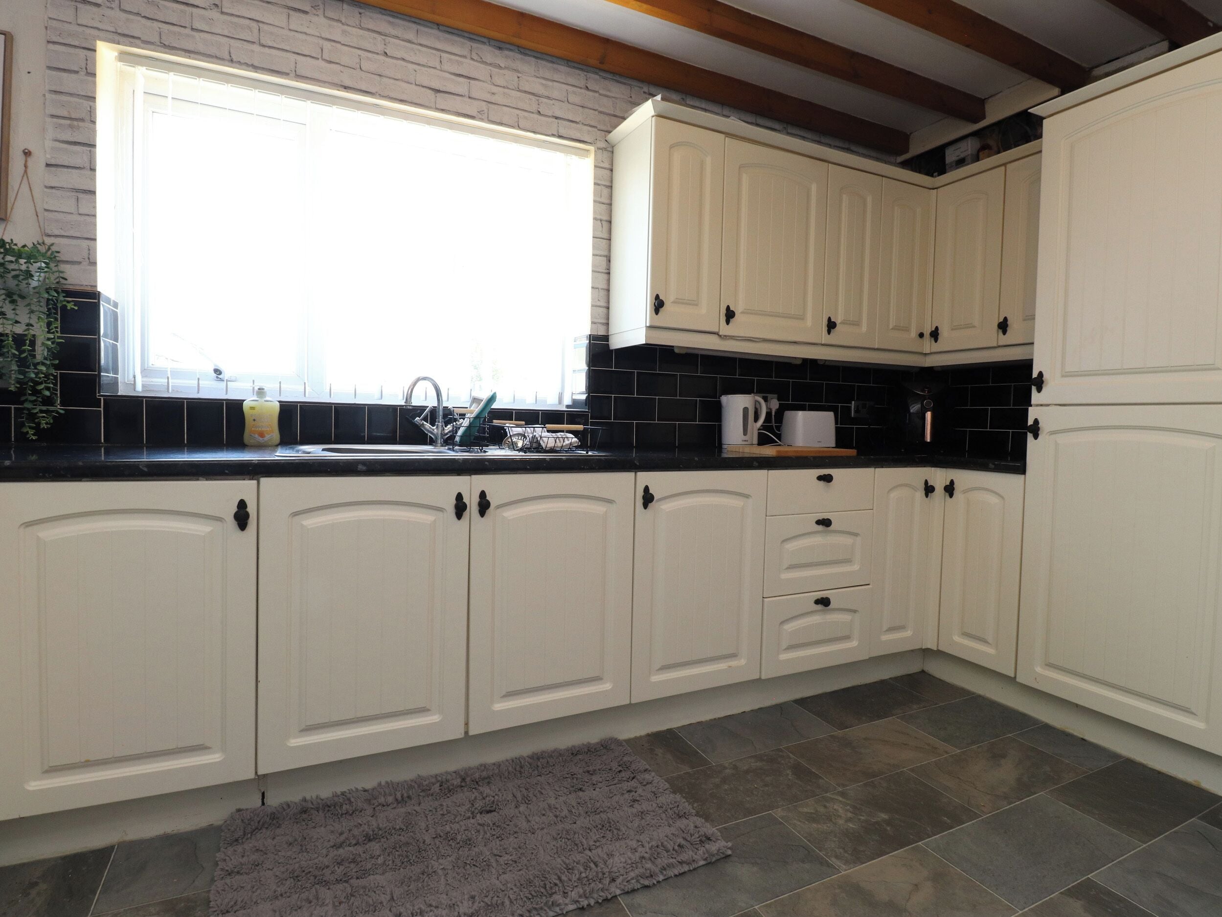 Una cocina con armarios blancos, encimera negra, ventana y alfombra gris.