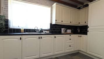 Una cocina con armarios blancos, encimera negra, ventana y alfombra gris.