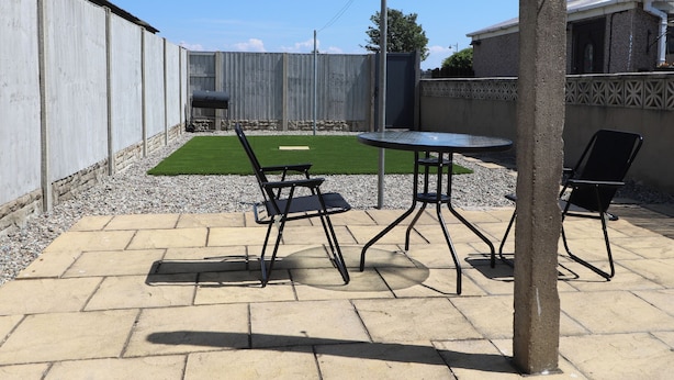Un patio con mesa y sillas, una parrilla y un jardín cercado.