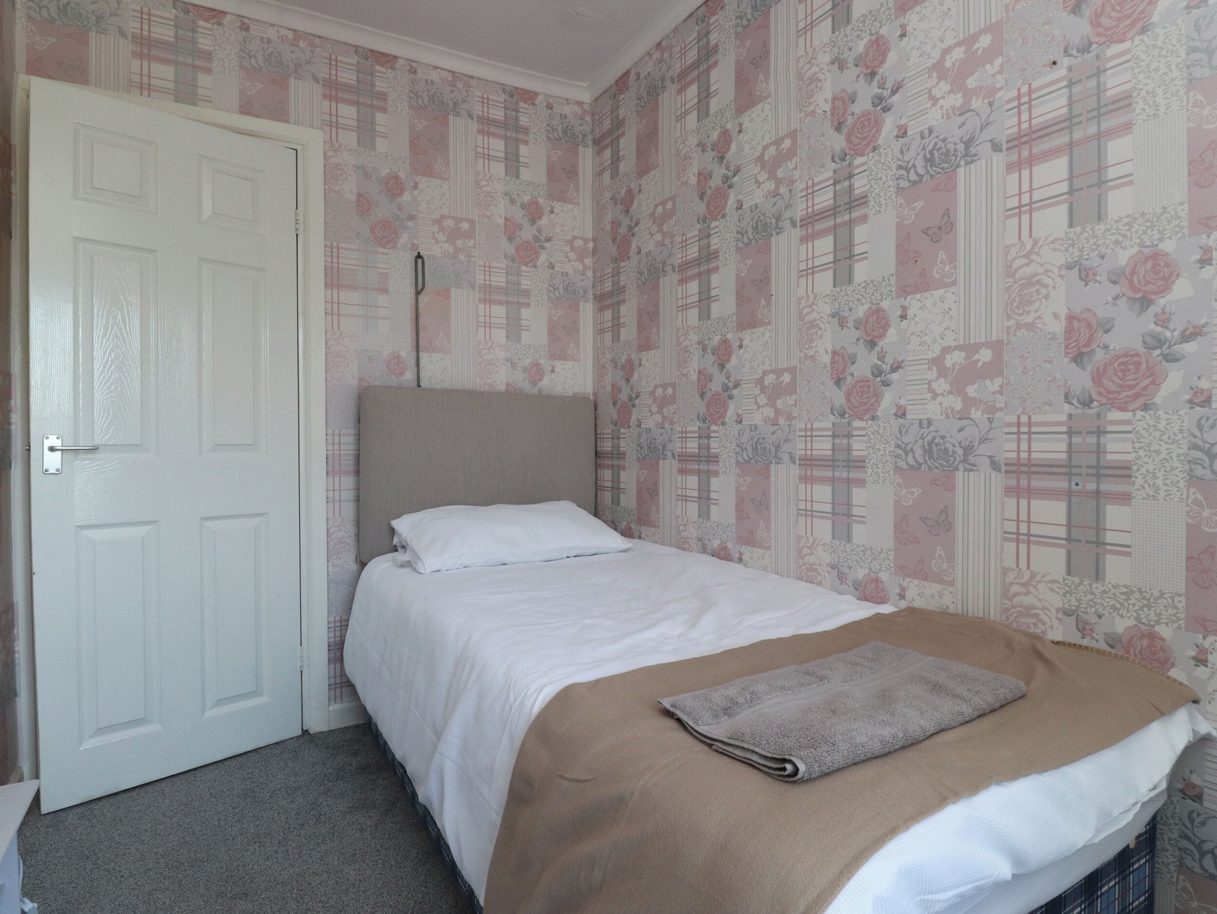 Un dormitorio con cama, una puerta y papel tapiz con motivos florales.