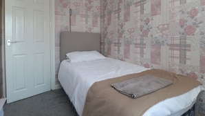 Un dormitorio con cama, una puerta y papel tapiz con motivos florales.