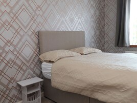 Una cama bien tendida con cabecera, una mesita de noche y un papel tapiz estampado.