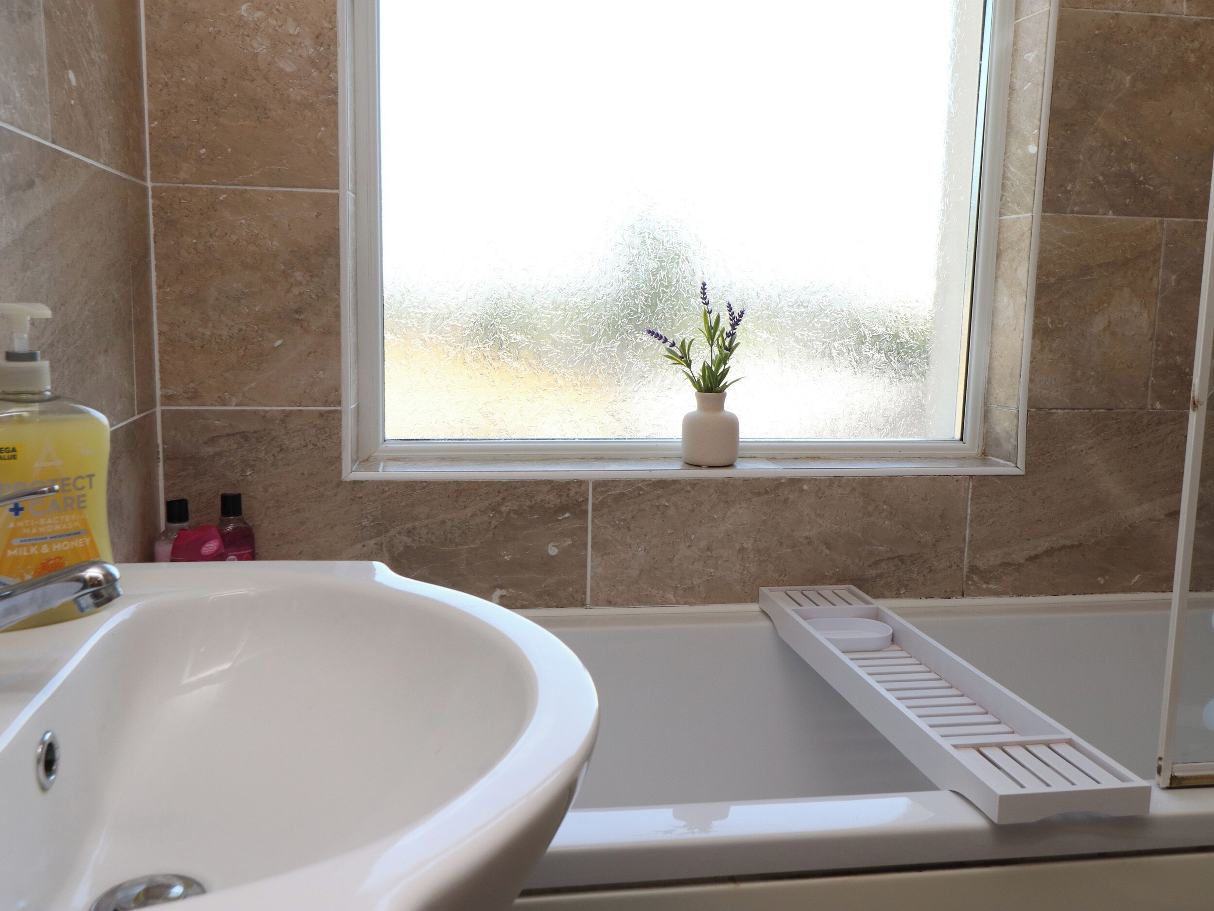 A bathroom with a white sink, a window with frosted glass, and a potted plant on the windowsill.
