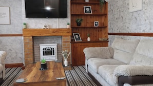 Una sala de estar con chimenea, un televisor montado encima, un sofá y una mesa de centro.