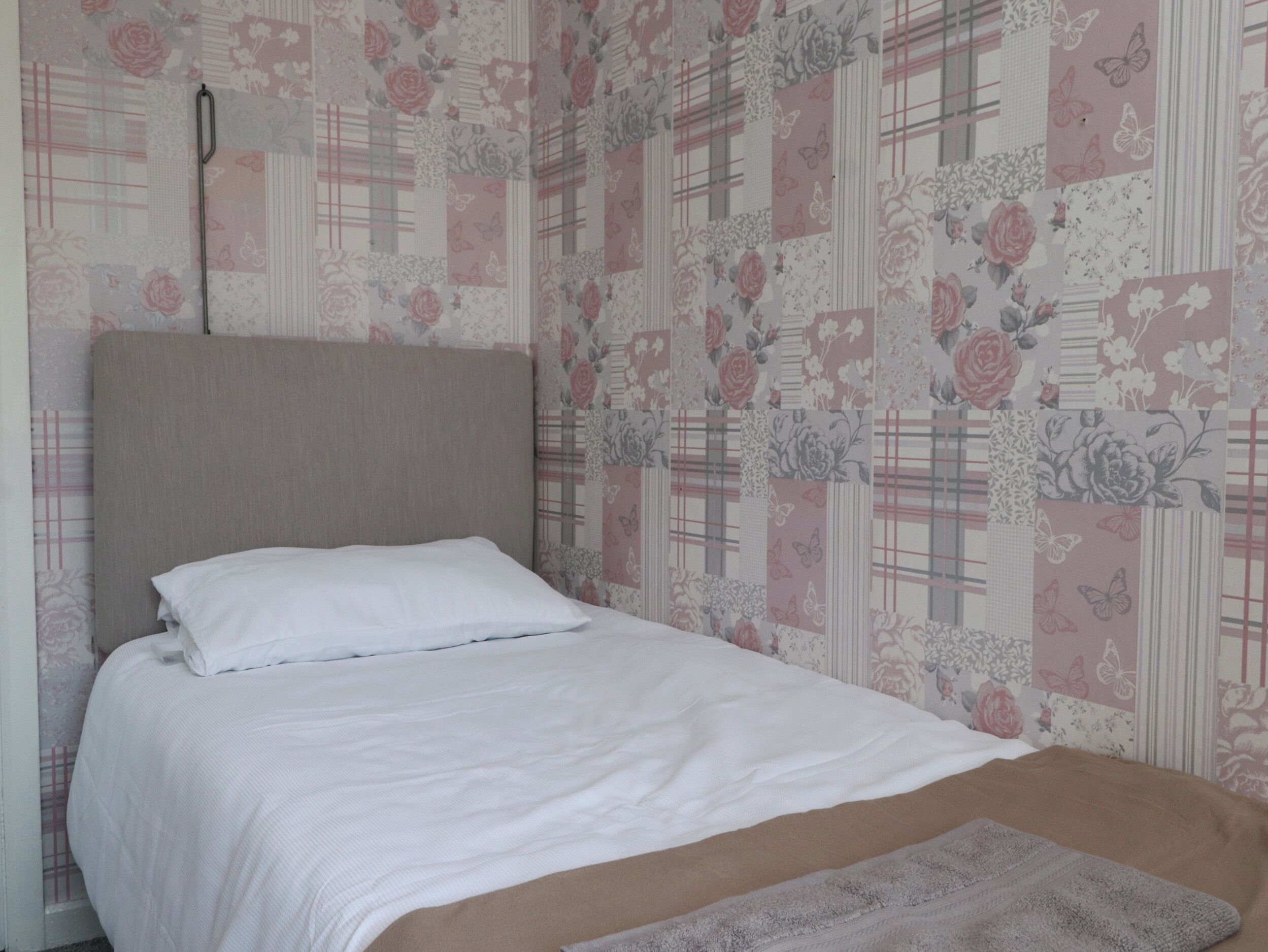 Una cama individual con cabecera, ropa de cama blanca y un papel tapiz floral estampado.