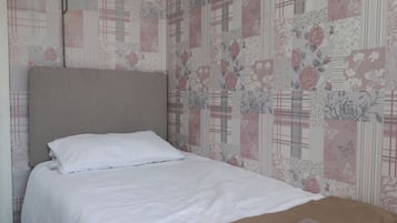 Una cama individual con cabecera, ropa de cama blanca y un papel tapiz floral estampado.