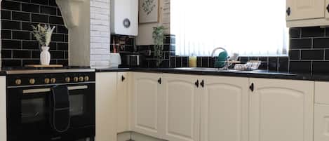 Una cocina con armarios blancos, estufa negra y ventana con persianas.