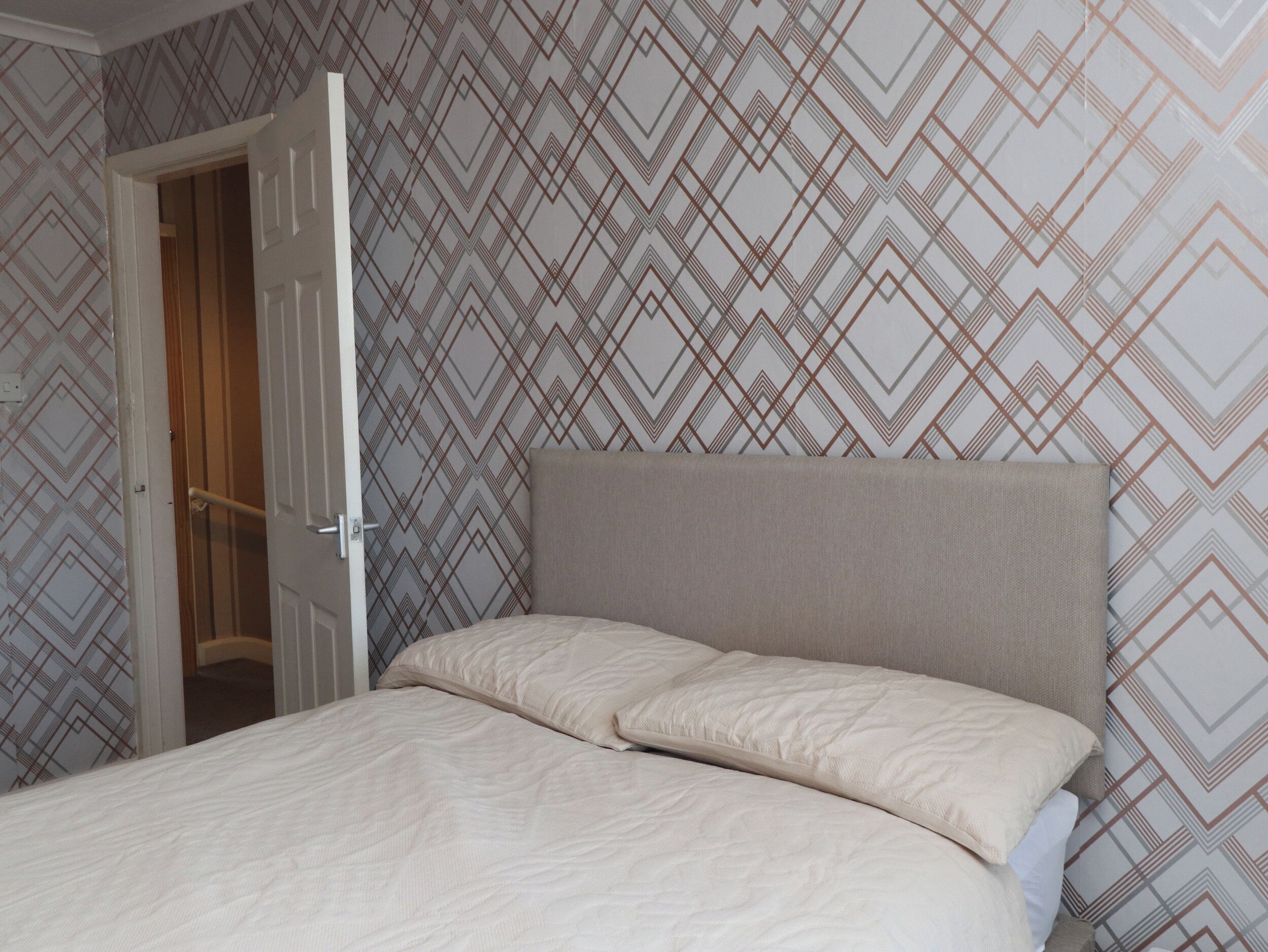 A bedroom with a bed, a door, and patterned wallpaper.