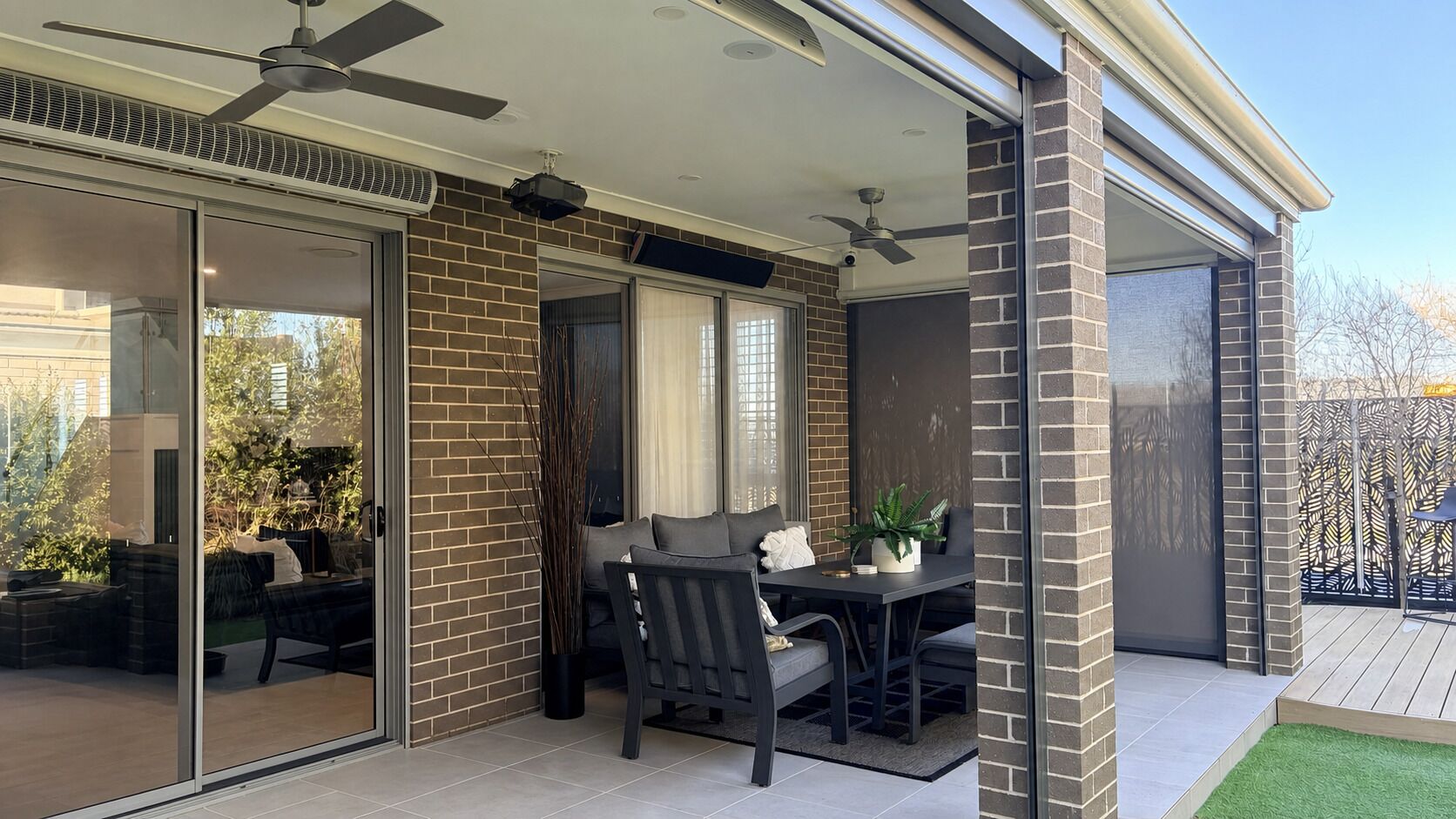 Un patio couvert avec une table et des chaises, un ventilateur de plafond et une vue sur l’extérieur.