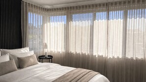 Une chambre d’hôtel avec un grand lit, une table de chevet avec une lampe et des rideaux légers.