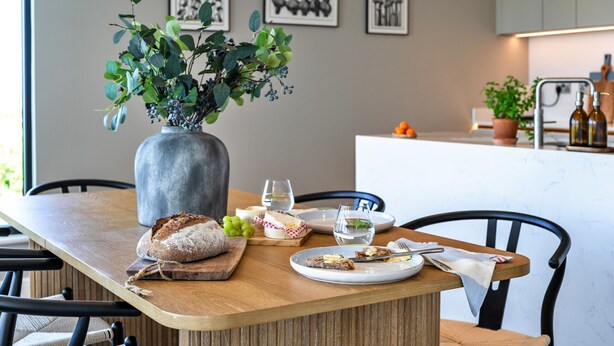 Una mesa de comedor con un jarrón de follaje verde, un pan y platos con restos de comida.