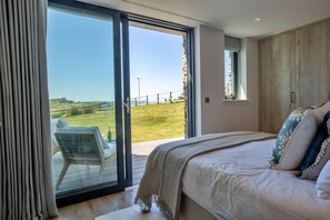A bedroom with a large bed, a view of a grassy area, and a sliding glass door leading to an outdoor seating area. - Perrantide (Upton)