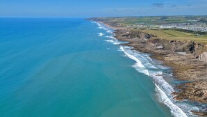 Un paisaje costero con playa, acantilados y un pueblo a lo lejos.