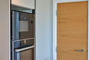 A kitchen with a built-in oven and microwave, a wooden door, and a stainless steel handle. - Perrantide (Upton)