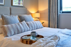 A neatly made bed with pillows, a tray with a mug and papers, a lamp, and curtains. - Perrantide (Upton)