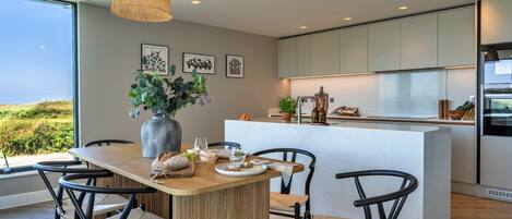 A modern kitchen with a central island, dining chairs, and pendant lighting.