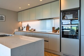 A modern kitchen with white cabinetry, a marble countertop, and a built-in oven. - Perrantide (Upton)