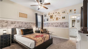 Une chambre à coucher comprenant un lit, un ventilateur de plafond, une table de chevet, une commode et une porte sur laquelle est inscrit « EXIGENCES RELATIVES À LA CHAMBRE ».
