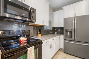 A modern kitchen with stainless steel appliances, white cabinets, and a tiled backsplash. - 1576 Flange Drive (Davenport)