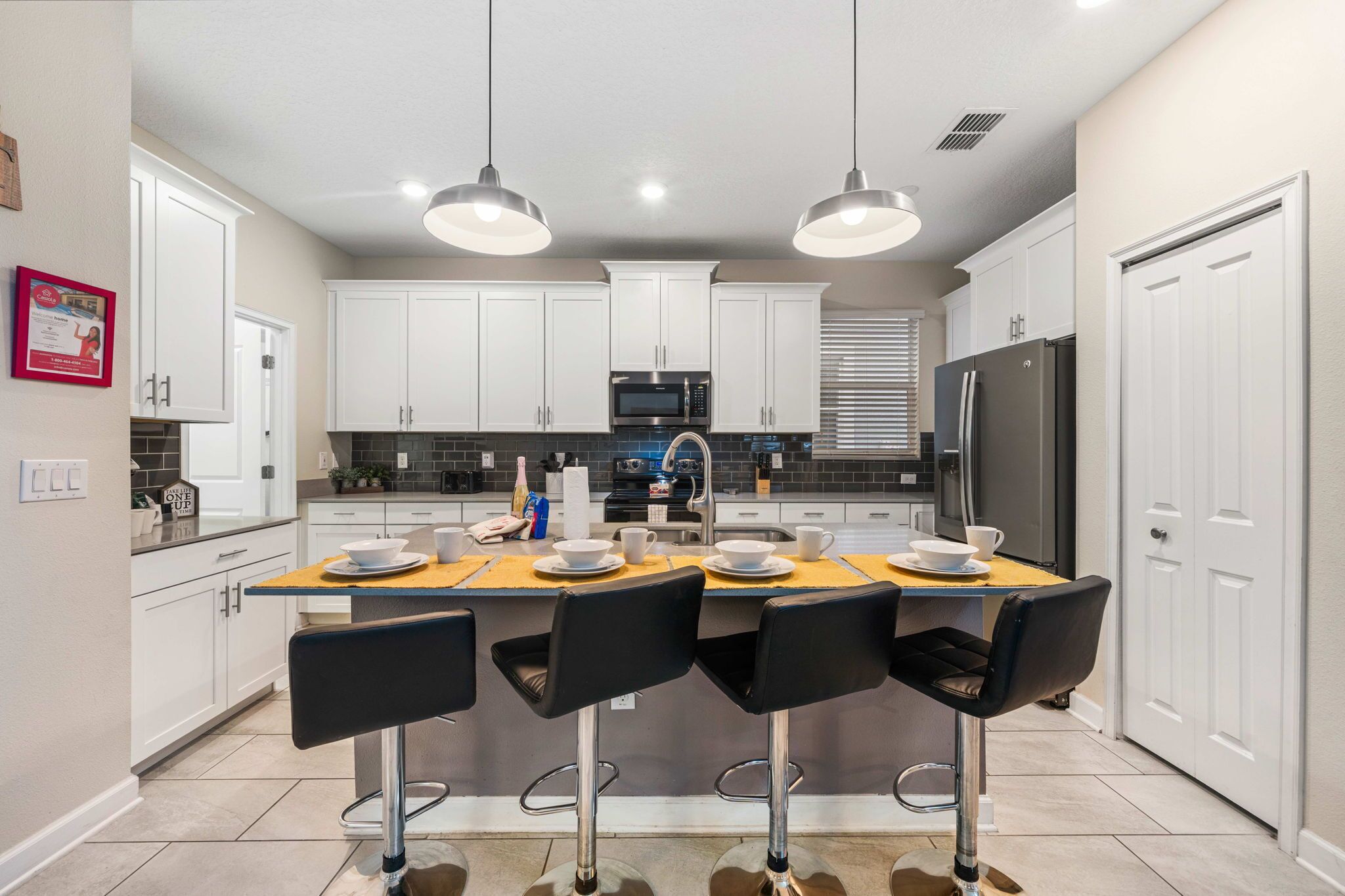 A modern kitchen with white cabinets, a central island with bar stools, and a stainless steel refrigerator.