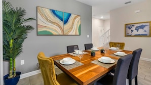 Un coin repas avec une table en bois, des chaises et un grand tableau abstrait accroché au mur.