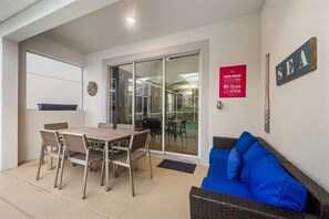 A covered patio area with a table and chairs, a glass door leading to a pool, and a sign with pool rules. - 1576 Flange Drive (Davenport)
