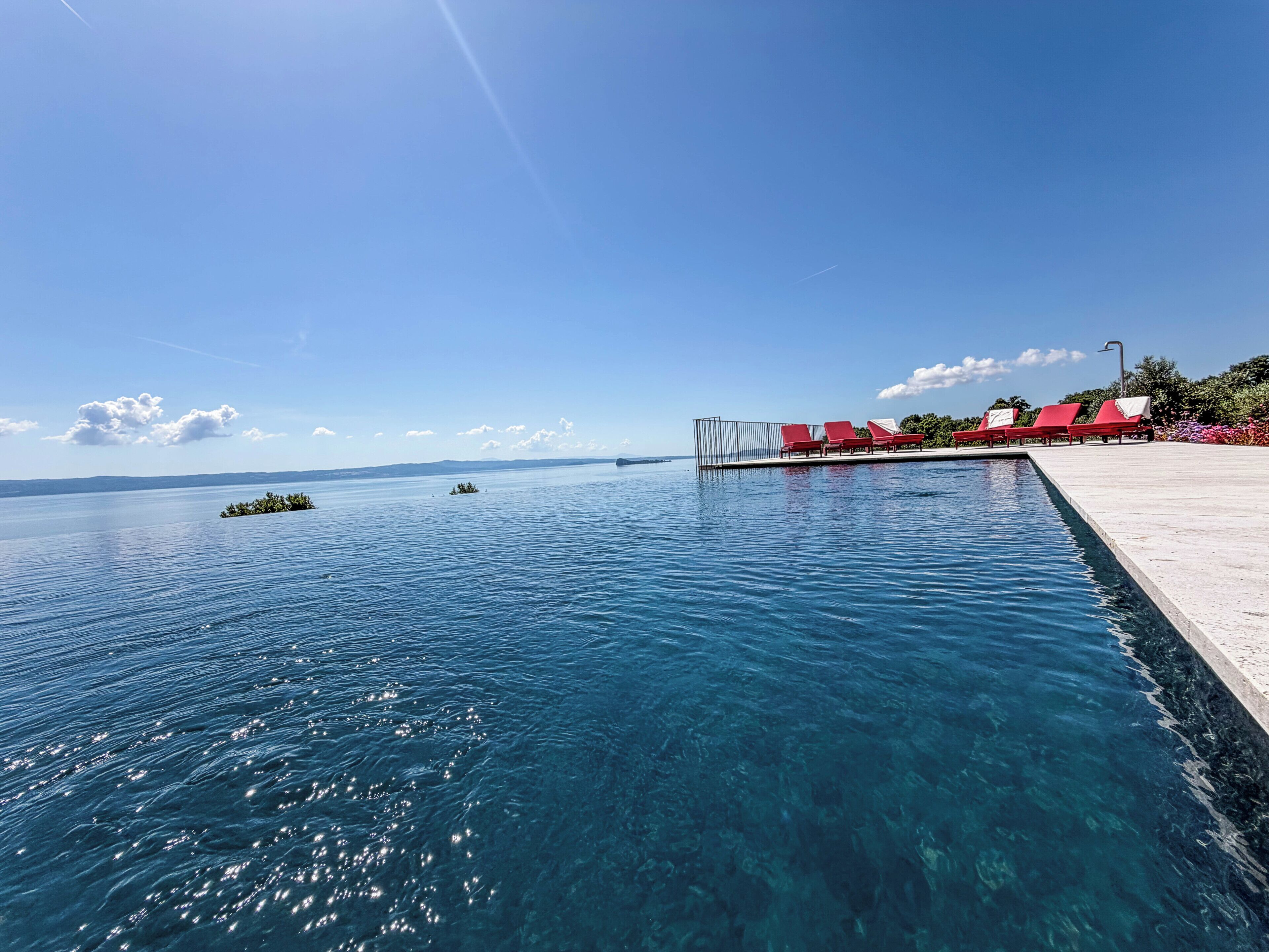 A clear blue pool with red lounge chairs and a view of the sea.