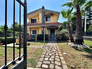 A two-story house with a stone pathway leading to the entrance, surrounded by greenery and palm trees. - Villa dell'Etna - Country Residence - (Mascalucia)
