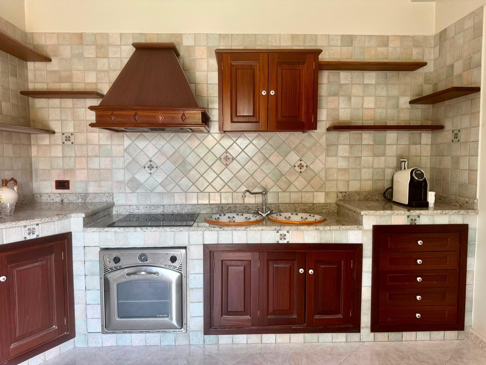 Uma cozinha com forno embutido, fogão, armários de madeira e painel de azulejos.