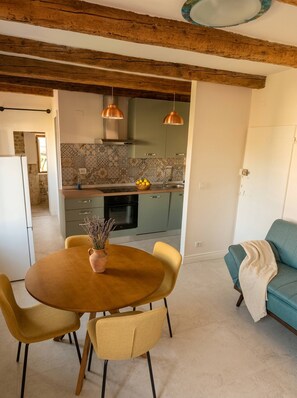A dining area with a wooden table and chairs, a vase with flowers, and a kitchen in the background.