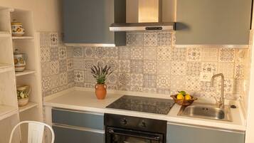 A kitchen with a built-in oven, a sink, and a stove. There is a potted plant on the counter and a bowl of fruit.