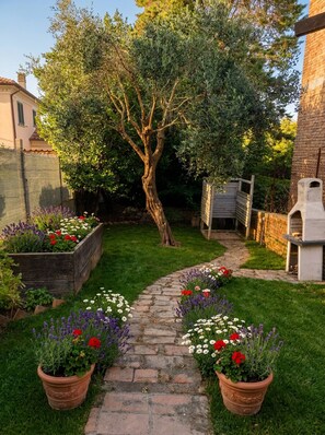 Un sentier de jardin qui mène à un arbre, entouré de parterres de fleurs et d’un mur de briques.