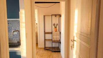 A hallway with a wooden floor, a metal shelf unit, and a white door.