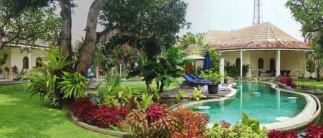 A swimming pool surrounded by lush greenery and a building with a tiled roof.