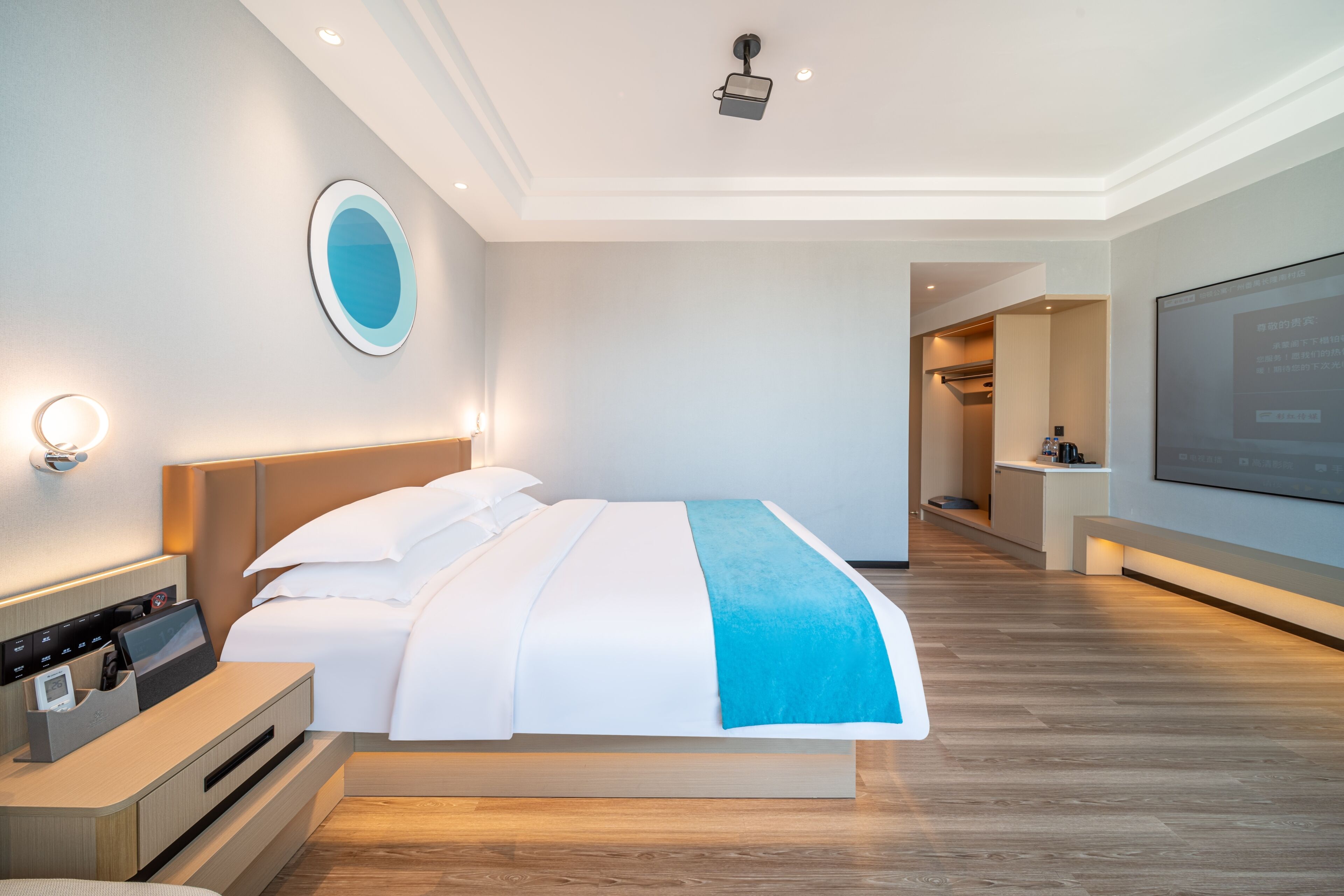 A modern hotel room with a large bed, bedside tables, a TV, and a bathroom visible in the background.